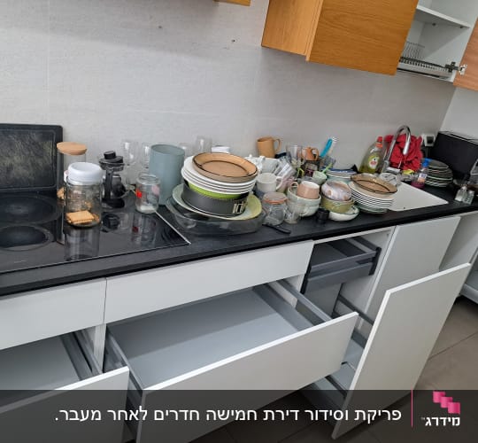 כלים מלוכלכים על השיש במטבח עם ארונות פתוחים